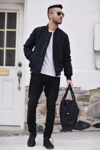 Мужчина в черной куртке, белой футболке, черных брюках и с сумкой в руке