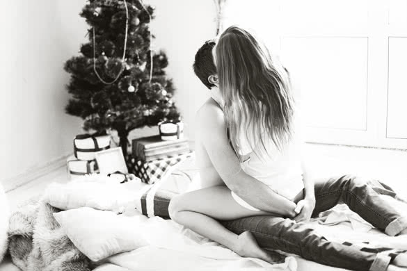 Young sweet pretty couple in love kissing in christmas eve near tree with gifts at home in december